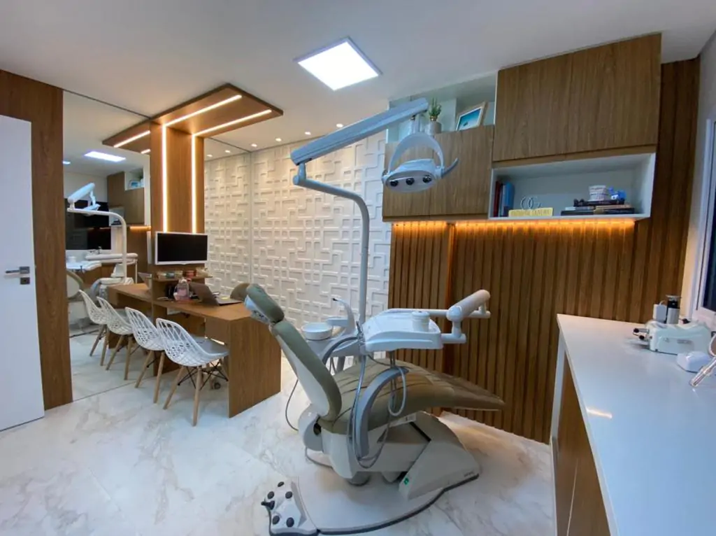 Vista completa do consultório, com cadeira odontológica, bancada e mesa de atendimento