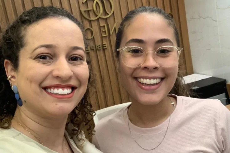 Doutora e paciente de óculos sorrindo juntas na clínica
